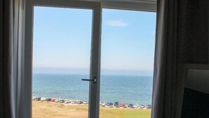 A room with a large window overlooking a beach and the sea. - Poseidon's Inn (Lossiemouth)