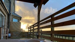A hot tub area with a wooden deck and a stone wall, overlooking a sunset. - Poseidon's Inn (Lossiemouth)