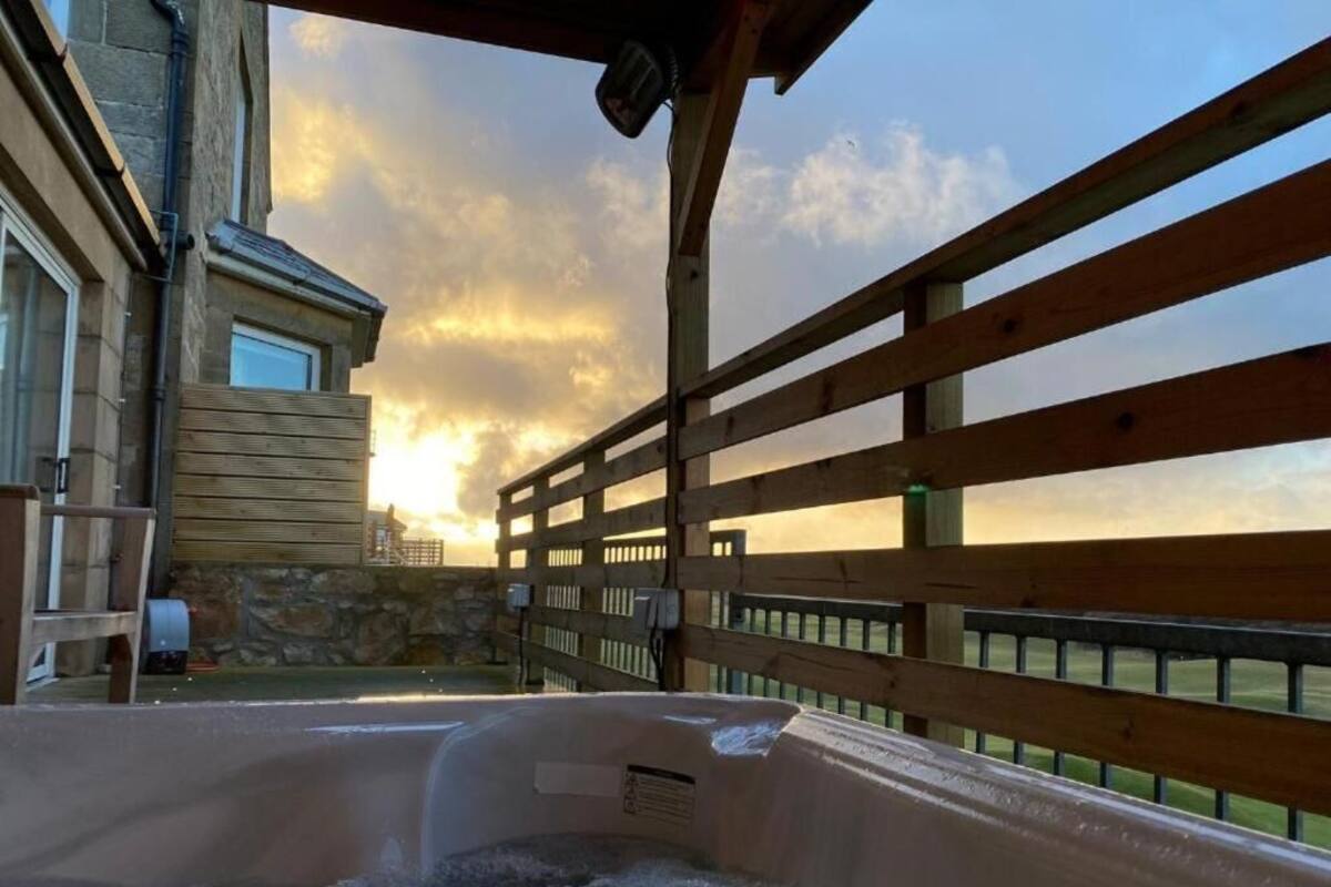Área de hidromassagem com deck de madeira e parede de pedra, com vista para um pôr do sol.