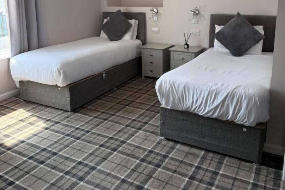 Quarto de hotel com duas camas, uma mesa de cabeceira, um espelho e uma janela com cortinas.