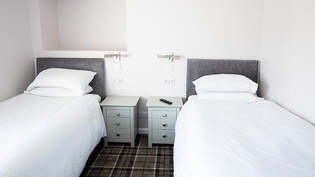 A twin room with two single beds, each with a grey headboard, white bedding, and bedside tables with drawers. - Poseidon's Inn (Lossiemouth)