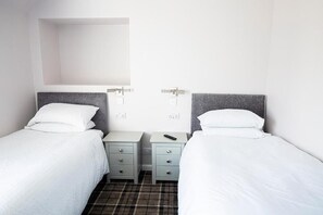 A twin room with two single beds, each with a grey headboard, white bedding, and bedside tables with drawers. - Poseidon's Inn (Lossiemouth)