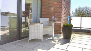 A balcony with a wicker chair and table, a potted plant, and a glass door leading to a room. - Refugium 1 (Emsdetten)
