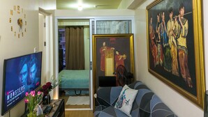 A living room with a television, a painting, and a clock on the wall. - Cozy LUZZO HOME 1-br luxury condo in  Kapitolyo pasig area 2mins away from BGC (Pasig)