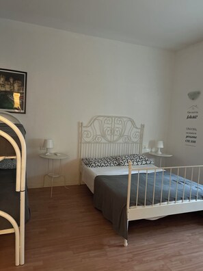 A bedroom with a metal bed frame, a bedside table with a lamp, a small round table with a lamp, and a wall with a decorative item and text. - B&B Topaze (Sirmione)