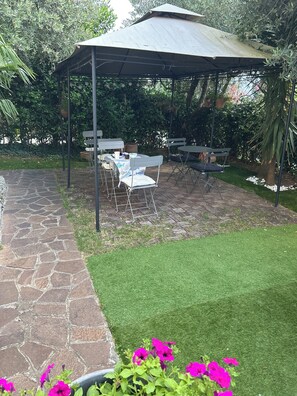 A covered patio area with stone flooring, a grassy lawn, and outdoor furniture. - B&B Topaze (Sirmione)