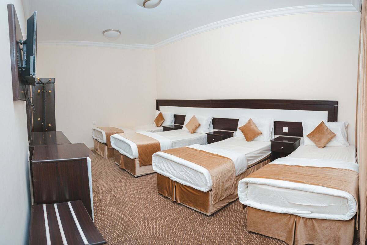 A hotel room with four single beds, a desk, and a television.