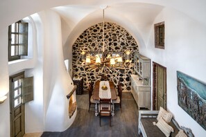 A dining area with a stone wall, a chandelier, and a table set for four. - Historical Villa Santa Croce (Santorini)