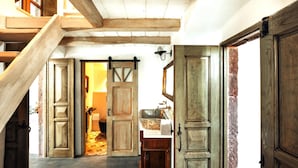 A wooden staircase leading to a room with a rustic interior, including a wooden door, a sink, and a hanging light fixture. - Historical Villa Santa Croce (Santorini)