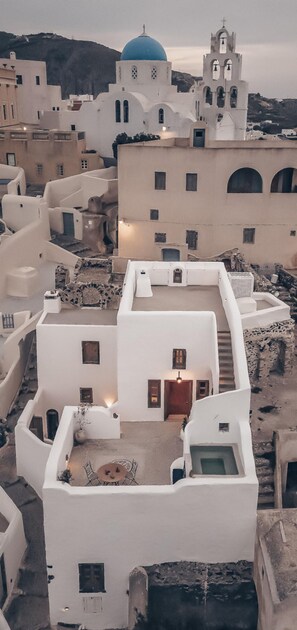 A white building with a blue dome and a bell tower, surrounded by other white buildings. - Historical Villa Santa Croce (Santorini)