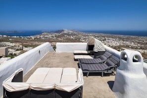 A rooftop terrace with sun loungers and a view of a coastal town. - Historical Villa Santa Croce (Santorini)