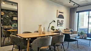 Een moderne woonkamer met een eethoek, met een houten tafel, grijze gestoffeerde stoelen, een zwarte vloerlamp en een grote spiegel.