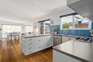 A modern kitchen with a central island, white cabinetry, and a blue-tiled backsplash. - Ohana Hale, Safety Beach. (Safety Beach)