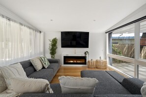 A modern living room with a fireplace, grey sofas, and a large TV. - Ohana Hale, Safety Beach. (Safety Beach)