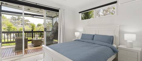 A bedroom with a bed, nightstands, a ceiling fan, and a view through a sliding glass door to an outdoor deck.