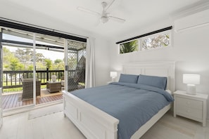 A bedroom with a bed, nightstands, a ceiling fan, and a view through a sliding glass door to an outdoor deck.