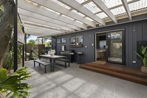 A covered patio with a grill, seating area, and a view of the backyard.