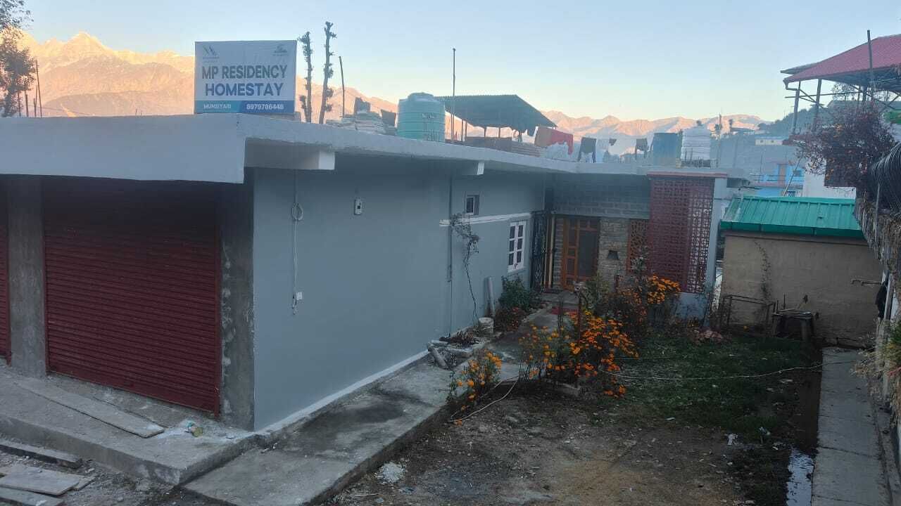 A building with a sign for 'MP Residency Homestay' and a small garden with orange flowers.