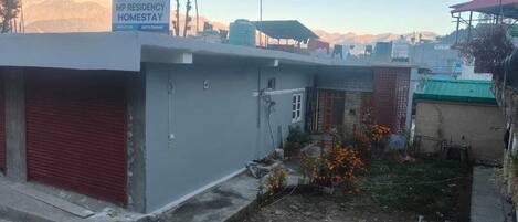 A building with a sign for 'MP Residency Homestay' and a small garden with orange flowers.