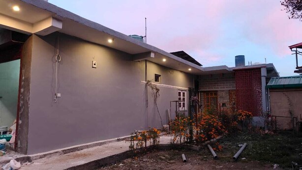 Un immeuble résidentiel à la façade grise, doté d’un petit jardin avec des fleurs oranges et d’un réservoir d’eau visible sur le toit.