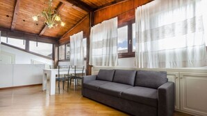 Un accogliente soggiorno con un divano grigio, pavimento in legno, un tavolo da pranzo con sedie e ampie finestre con tende.