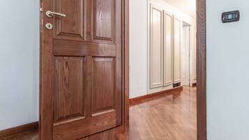 Una porta in legno con una serratura, un corridoio con pavimento in legno e un termostato fissato al muro.