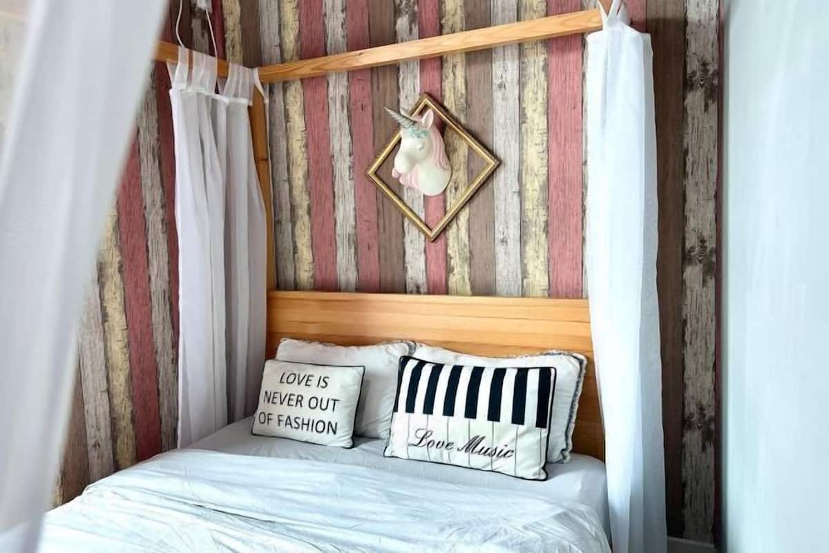 A bed with white bedding, two pillows with text, a wooden headboard, and a unicorn decoration.