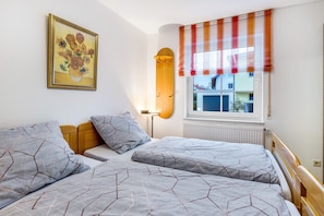 Ein Schlafzimmer mit zwei Betten, einem Nachttisch, einer Lampe, einem Fenster mit gestreiften Vorhängen und einem Bild an der Wand.