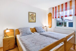 Un dormitorio con cama, mesitas de noche, lámpara, ventana con cortinas e imagen colgada en la pared.