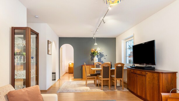 Una sala de estar con sofá, mesa de centro, televisor, zona de comedor con sillas y mesa, y un mueble aparador.