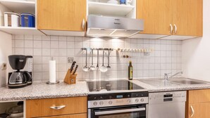 Una cocina moderna con armarios de madera, estufa de acero inoxidable, lavavajillas y una encimera con diversos utensilios de cocina.
