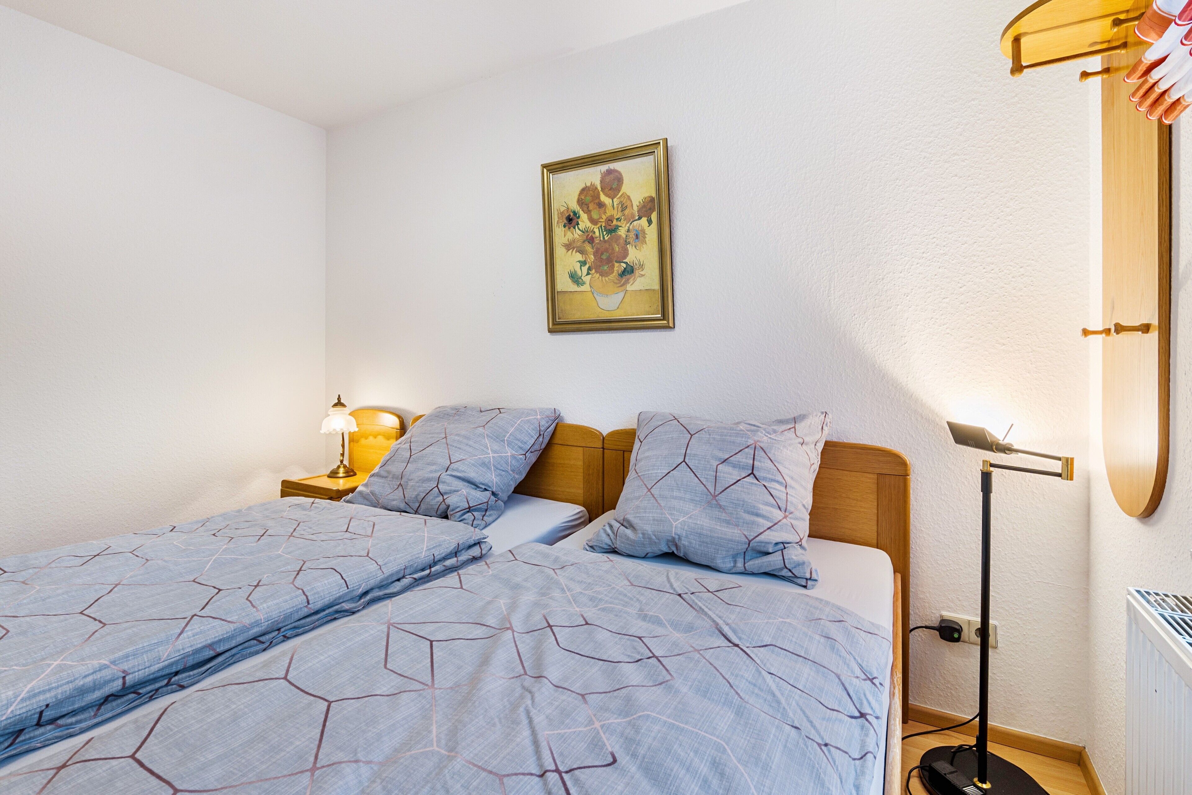 Een slaapkamer met een bed, nachtkastje, lamp en een schilderij aan de muur.