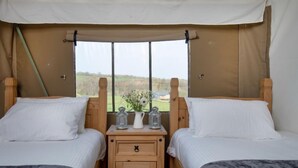 A tented room with two beds, a wooden nightstand with a vase and lanterns, and a view of the countryside. - Woodpecker at Kittisford Barton, Somerset with hot tub (Wellington)