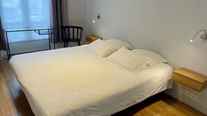 Ein ordentlich bezogenes Bett mit weißen Leinen in einem Zimmer mit Holzboden, einem kleinen Tisch und einem Stuhl.