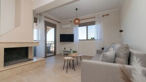 Ett modernt vardagsrum med en öppen spis, en soffa, en tv och utsikt över naturen.