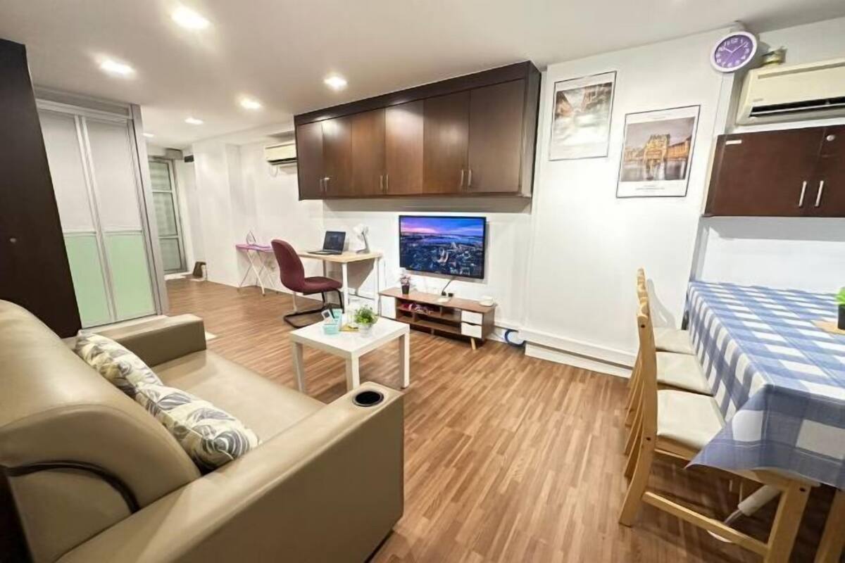 A modern living room with a sofa, a small table, a TV, and a dining area with a table and chairs.