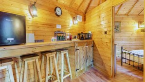 A wooden cabin interior with a kitchen area, bar stools, a bed, and a television. - Bears House, Cambridgeshire, with hot tub (Westley Waterless)