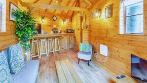 A cozy cabin interior with a wooden dining area, a bar, a sofa, a TV, and a plant. - Bears House, Cambridgeshire, with hot tub (Westley Waterless)