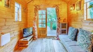 A cozy cabin with a wooden interior, a sofa, a TV, and a sliding door leading to an outdoor area. - Bears House, Cambridgeshire, with hot tub (Westley Waterless)