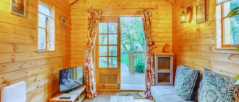 A cozy cabin with a wooden interior, a sofa, a TV, and a sliding door leading to an outdoor area.