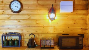 A wooden cabin interior with a clock, a lantern, a kettle, a toaster, and a microwave on the counter. - Bears House, Cambridgeshire, with hot tub (Westley Waterless)