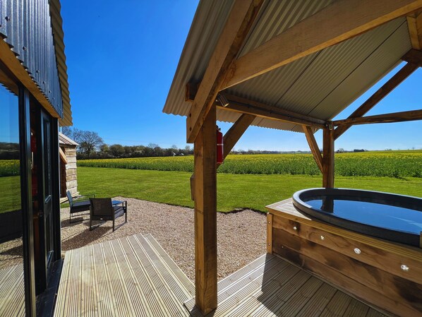 Une terrasse en bois avec un jacuzzi, un espace salon couvert et une vue sur un champ.