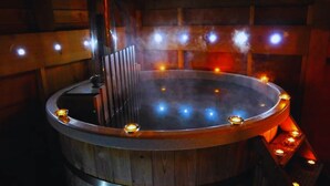 Ein Whirlpool mit Holzaußenverkleidung und Metallrand, umgeben von Kerzen.