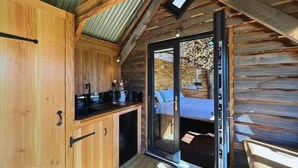 Ein Holzblockhaus-Innenraum mit einer Küchenzeile, einer Schiebetür zu einem Schlafbereich und einem kleinen Fenster.