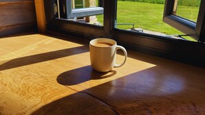 Eine Kaffeetasse auf einem Holztisch vor einem Fenster mit Blick auf ein Feld und ein Gebäude.