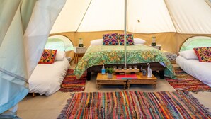 Uma tenda acolhedora com duas camas, tapetes coloridos e uma mesa pequena com objetos decorativos.