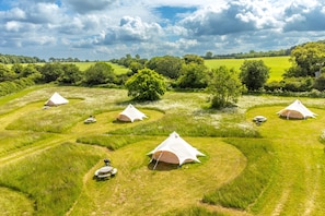 A campsite with multiple tents arranged in a circular pattern on a grassy field, surrounded by trees and open fields. - Daisy at Blanca’s Bell Tents, Hunstanton, Norfolk (Ringstead)