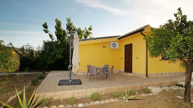 Un bâtiment jaune doté d’un patio, d’une table et de chaises, ainsi que d’une porte.