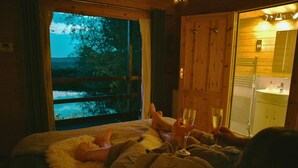 Een kamer met een bed, een raam met uitzicht op bomen en een houten deur.