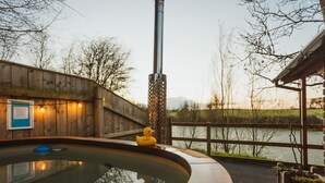 Een hottub met een houten terras, een houten omheining en uitzicht op een waterpartij.